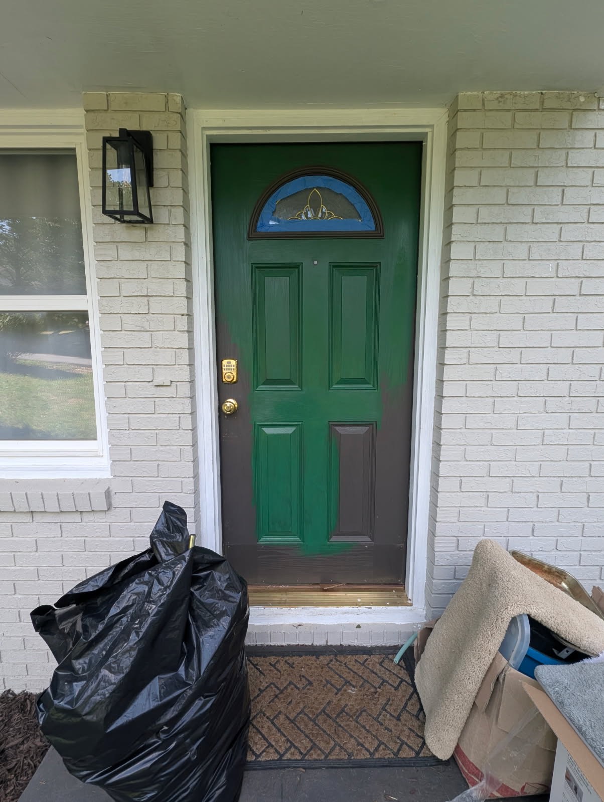 Front door mid-paint, green over brown, trash bags still on the porch.